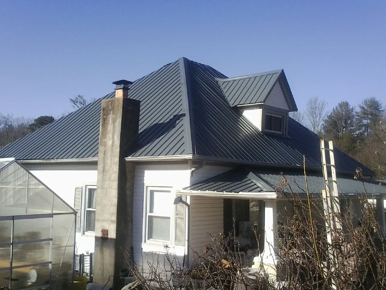 Dark blue standing seam metal roof on a white farmhouse with dormer — Slate & Tile Roof Repair by Roofing Brothers in Leeds