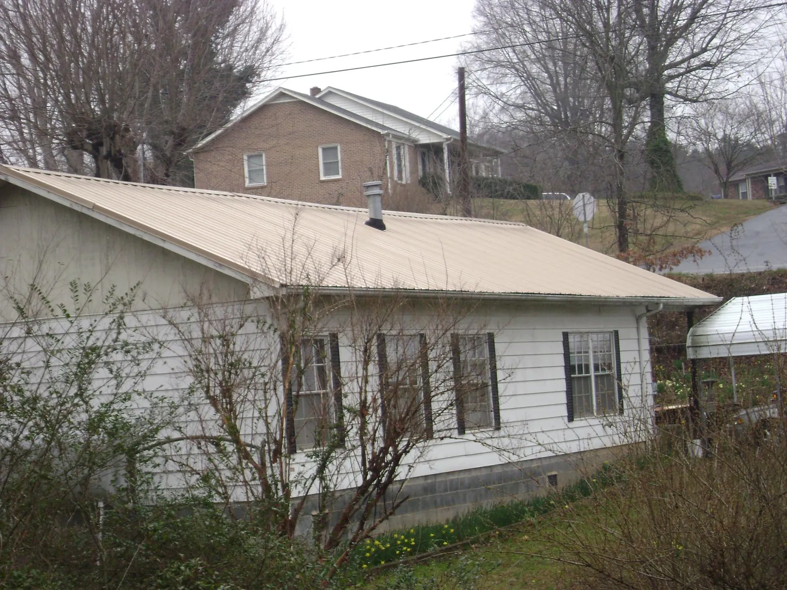 Tan metal roof on a white sided house set into a hillside — Commercial Roofing by Roofing Brothers in Leeds